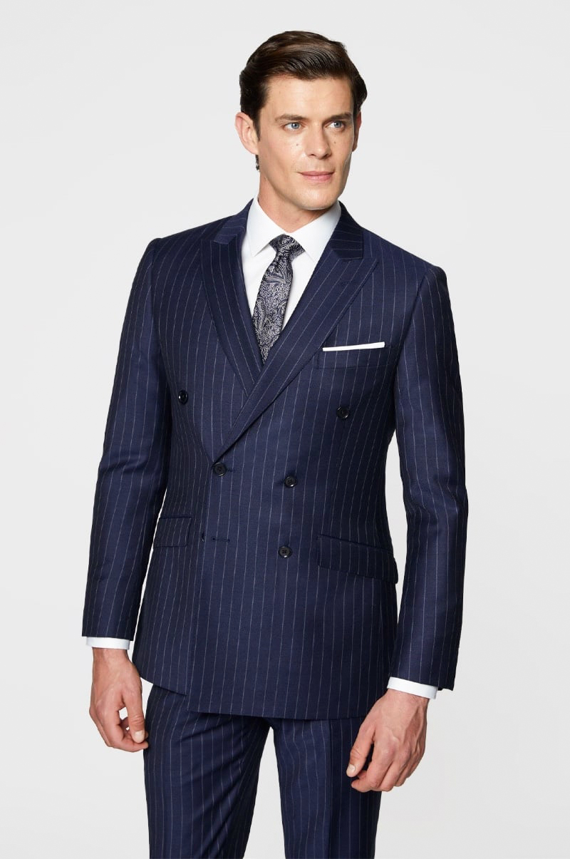 Model wears a navy pinstripe double-breasted suit with a white dress shirt and paisley tie