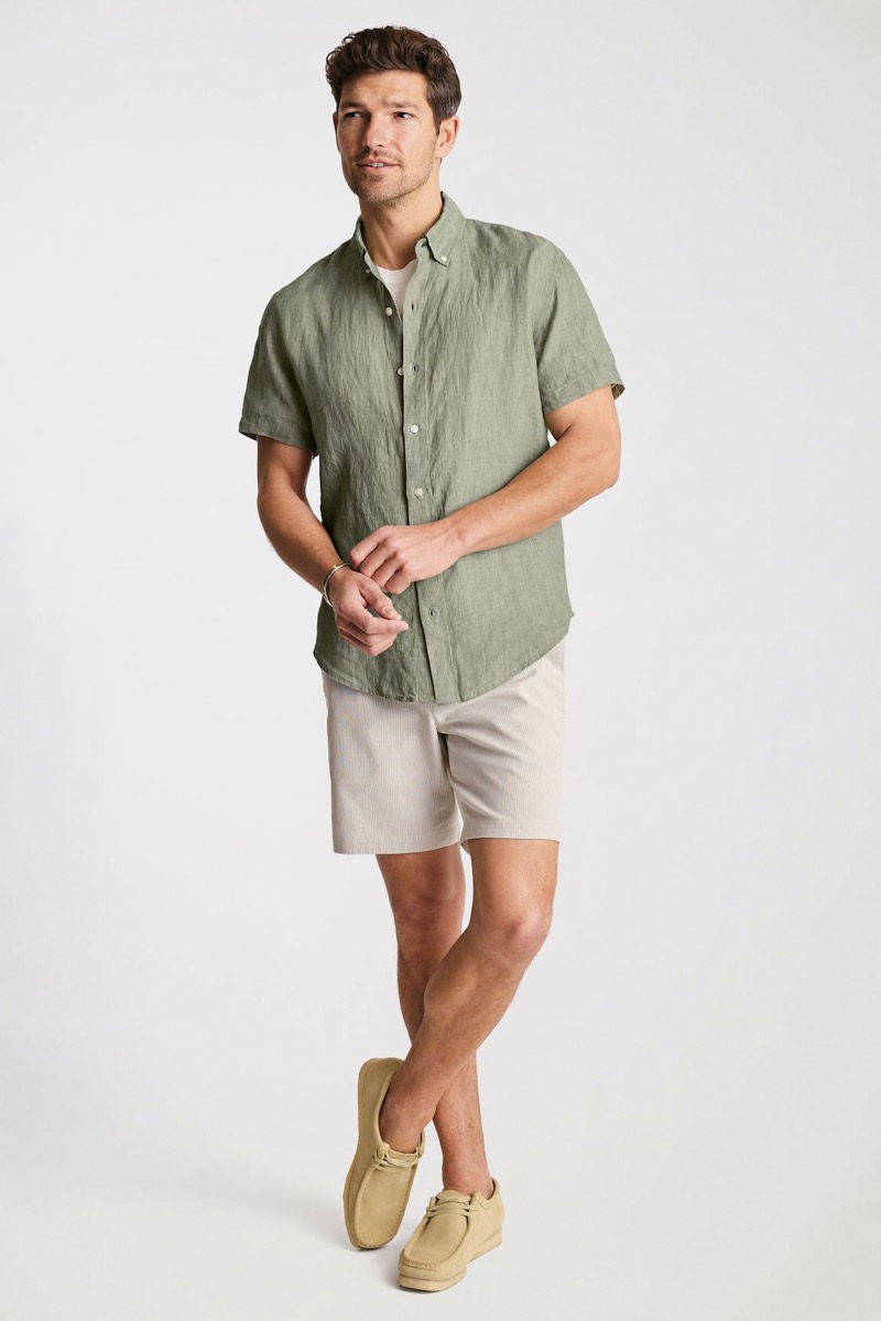 Model wears sage green short-sleeve linen shirt with shorts and wallabee boots