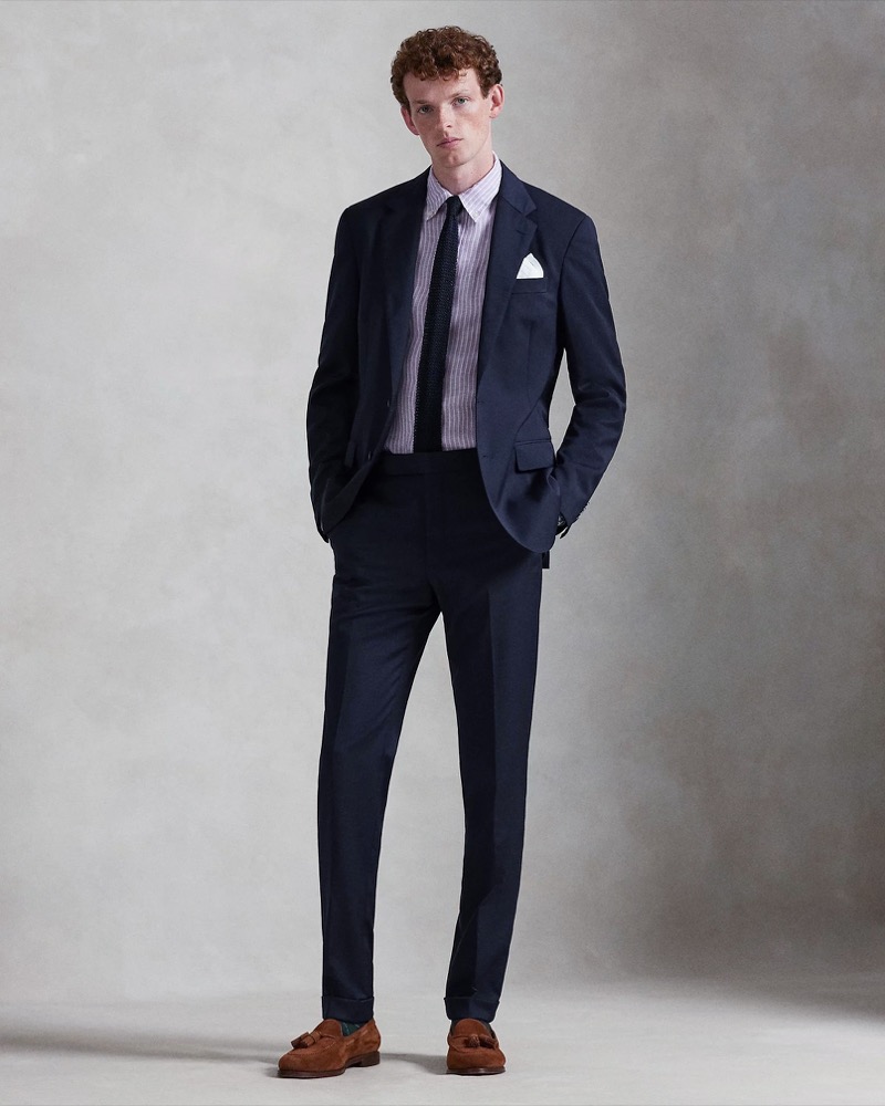 Model wears navy linen suit with striped shirt and brown tassel loafers