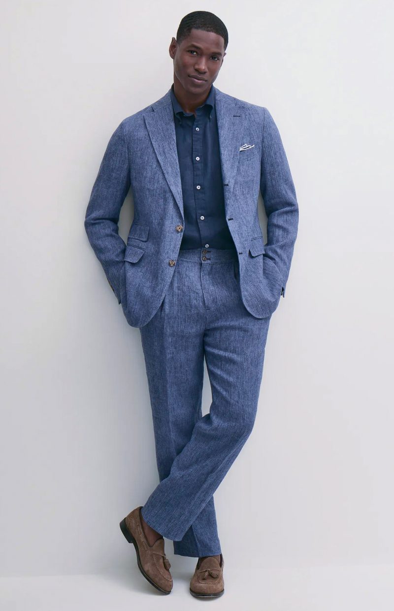 Model wears a blue linen suit with a navy shirt and brown suede tassel loafers