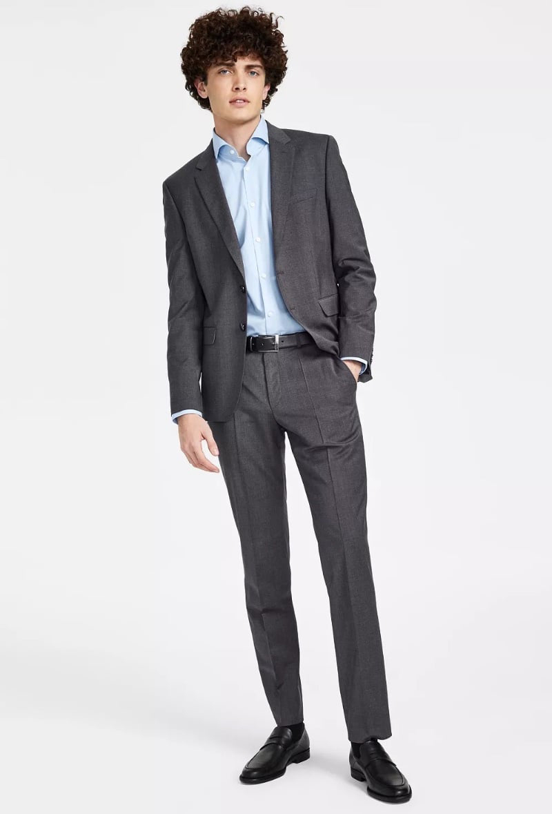 Model wears a dark gray modern-fit suit with a light blue dress shirt and black leather loafers
