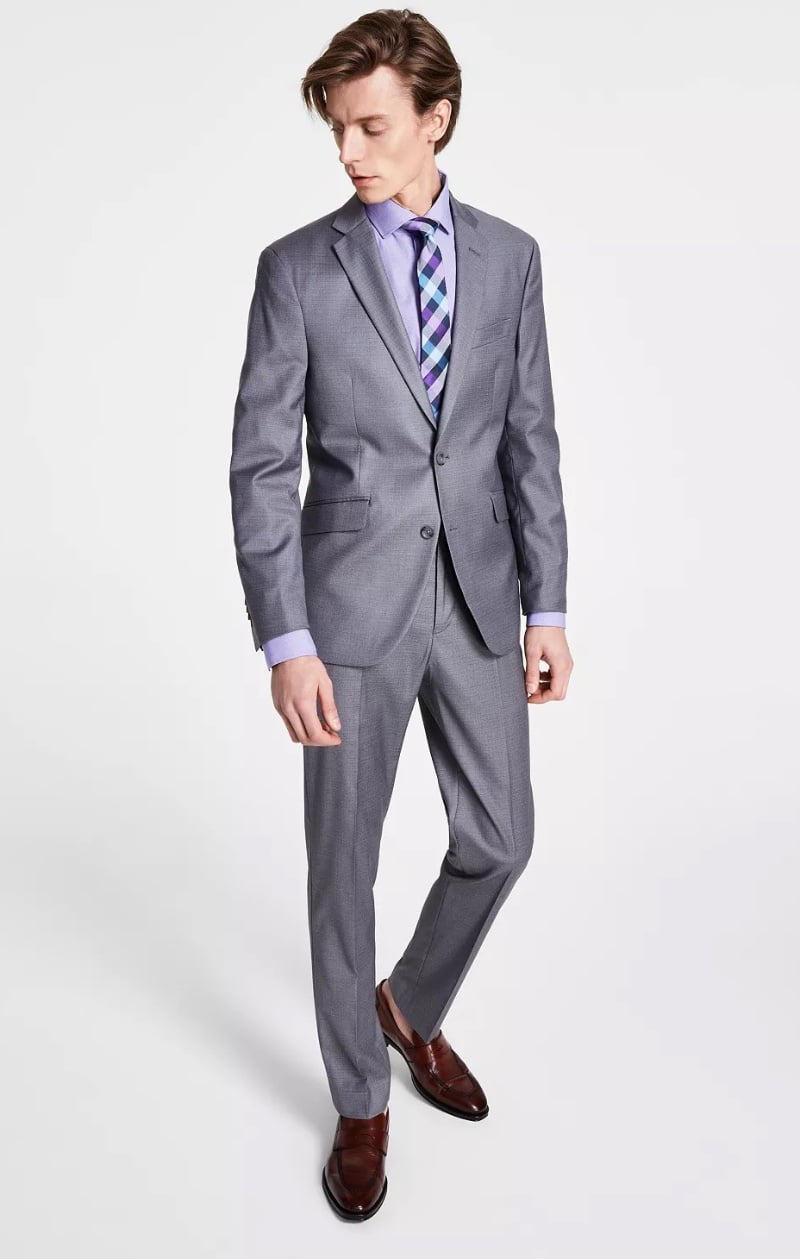 Model wears a slim-fit gray suit with a lavender dress shirt and brown leather loafers