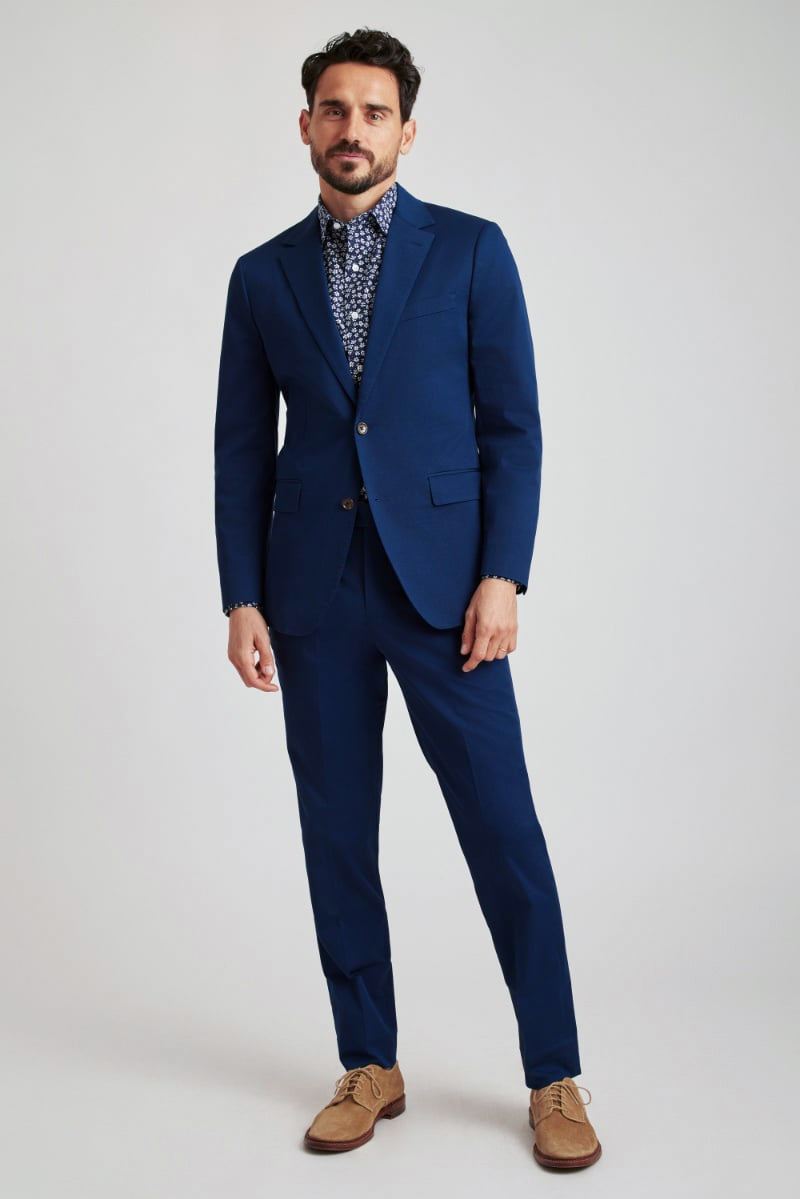 Model wears a two-piece navy suit with a floral print shirt
