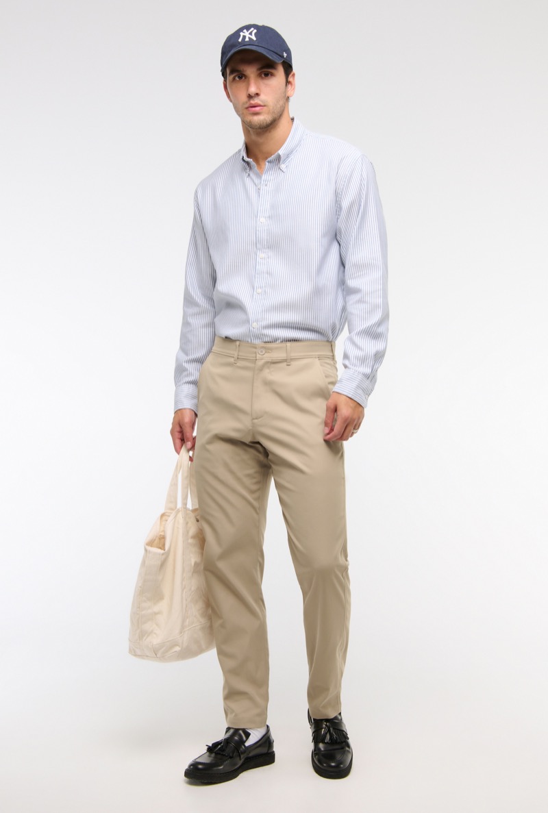 model wears striped oxford shirt with khaki chinos, baseball cap, and black leather tassel loafers