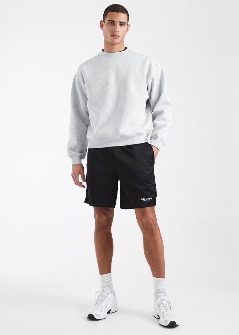 Man wearing black basketball shorts with a grey crewneck sweatshirt and white sneakers