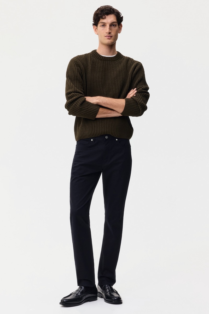 Man wearing slim black 5-pocket pants with chunky olive waffle knit crewneck sweater and black penny loafers