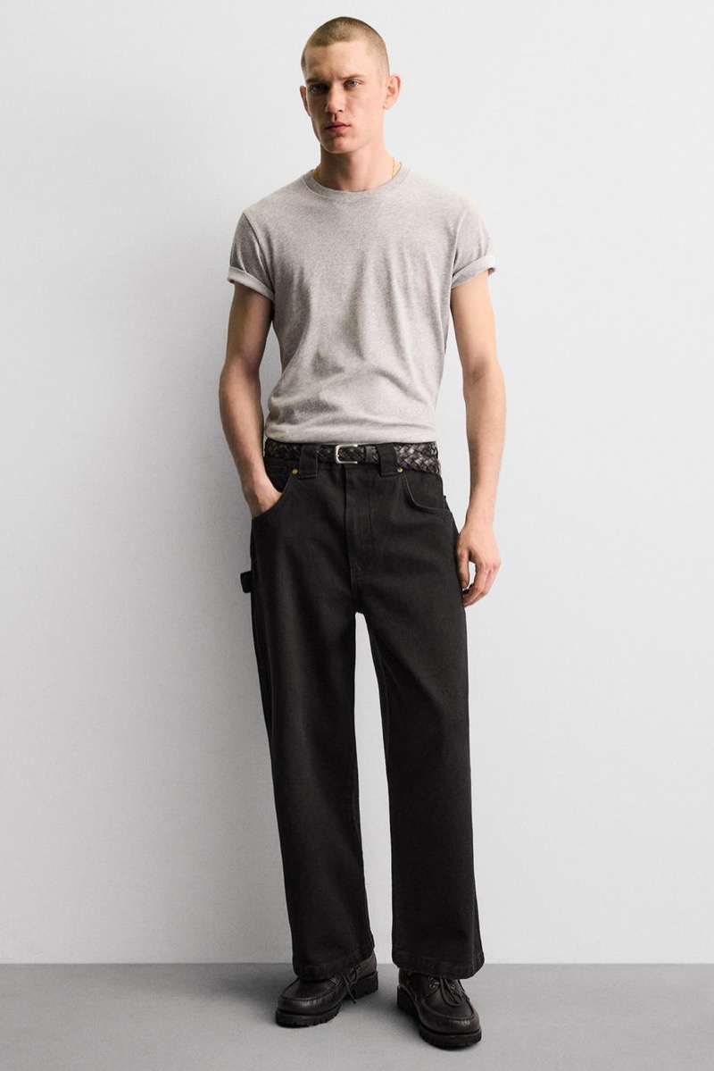 Man wearing wide-leg black carpenter pants with fitted gray cuffed T-shirt, woven black belt, and black boat shoes