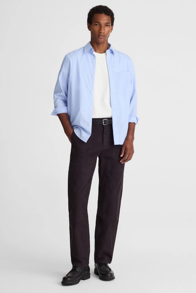 Man wearing relaxed black pants with light blue oxford cloth button-down untucked over white tee, black belt, and chunky black derby shoes