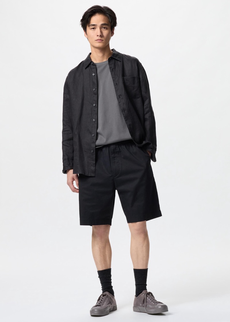 Man wearing black shorts with a dark linen button-down shirt and grey sneakers