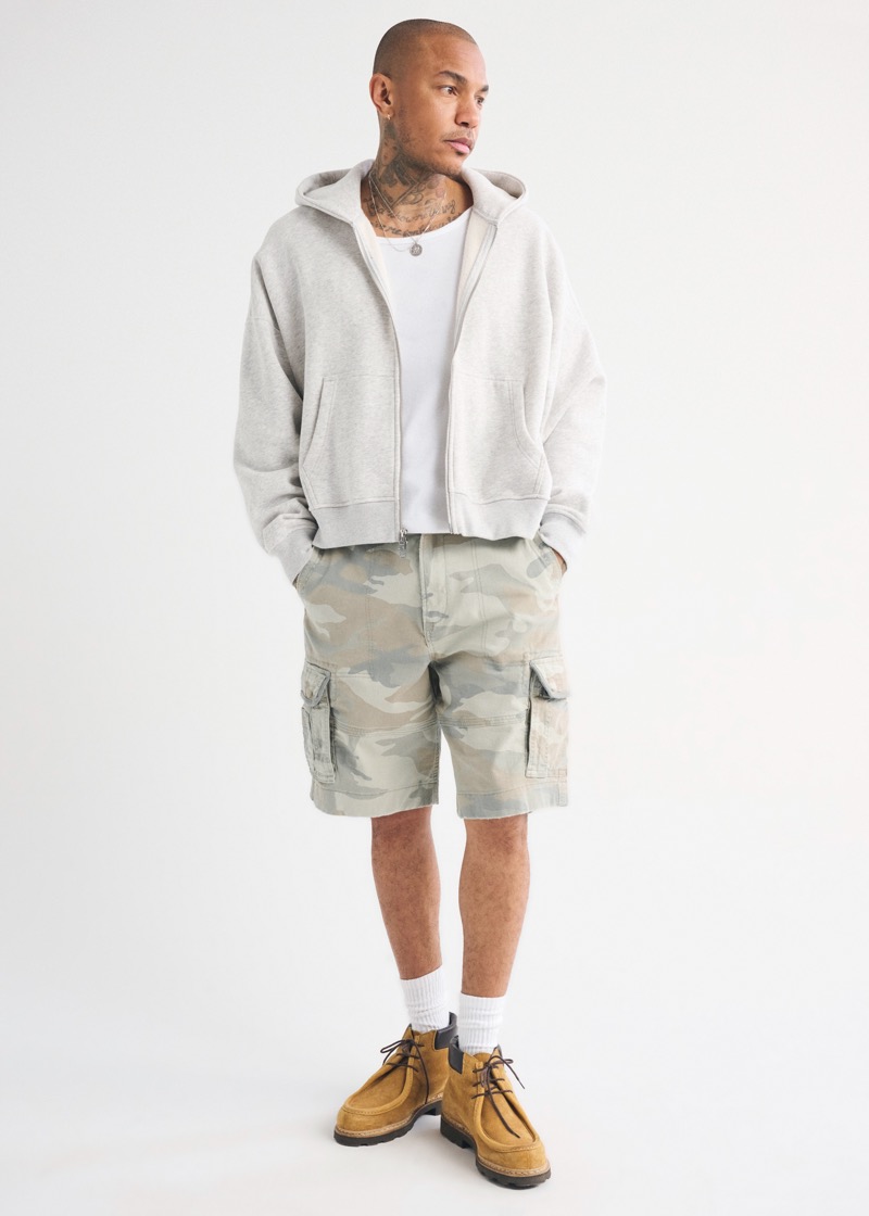 Man wearing camo cargo shorts with a grey zip-up hoodie and suede wallabee boots