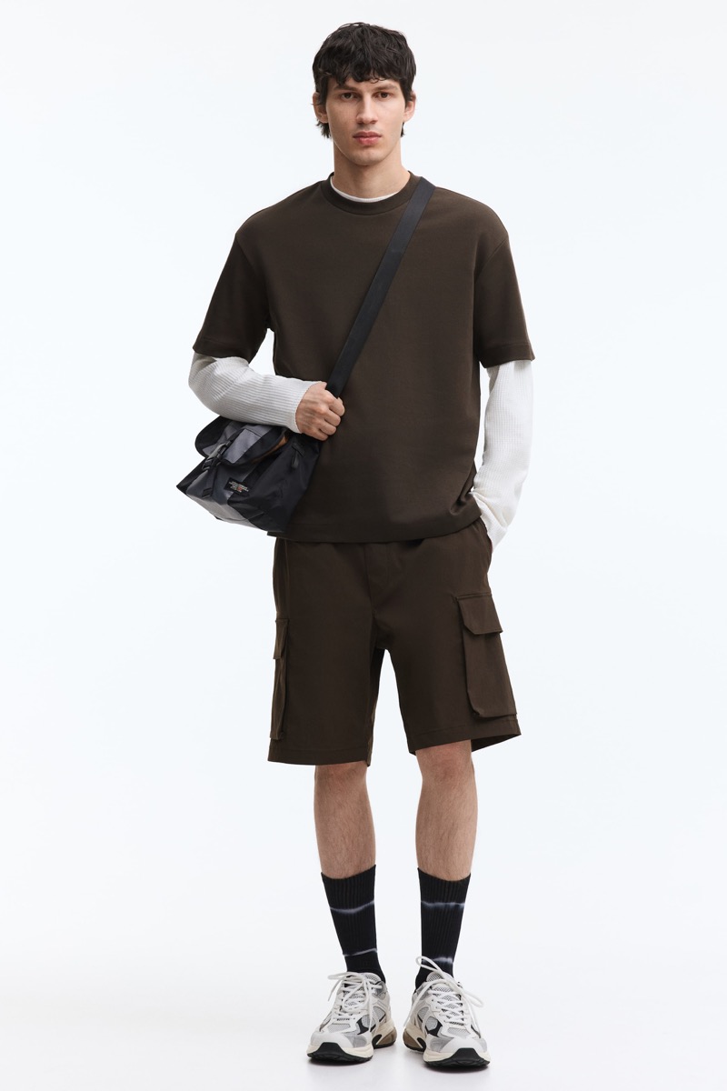 man wearing olive cargo shorts with a short-sleeve top layered over a thermal top and sneakers