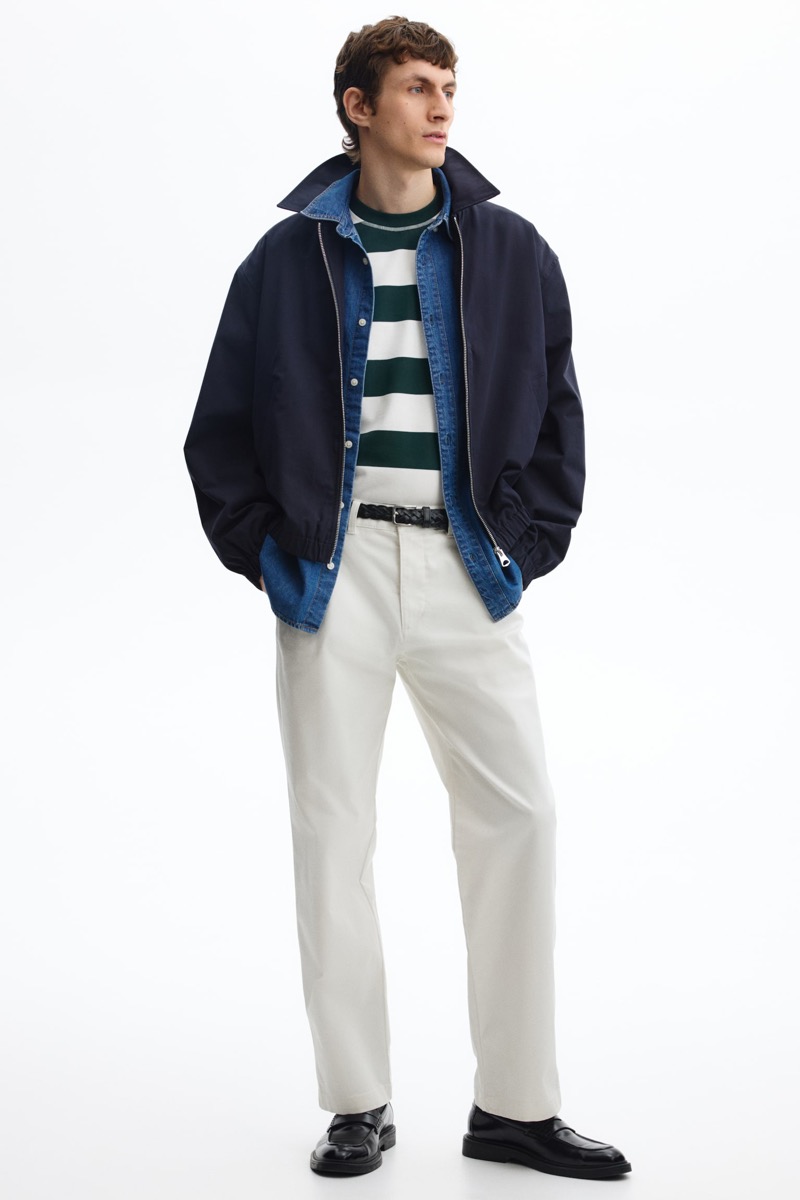 model wears chinos with a green and white striped t-shirt, denim shirt, navy bomber jacket, black braided leather belt, and black leather loafers