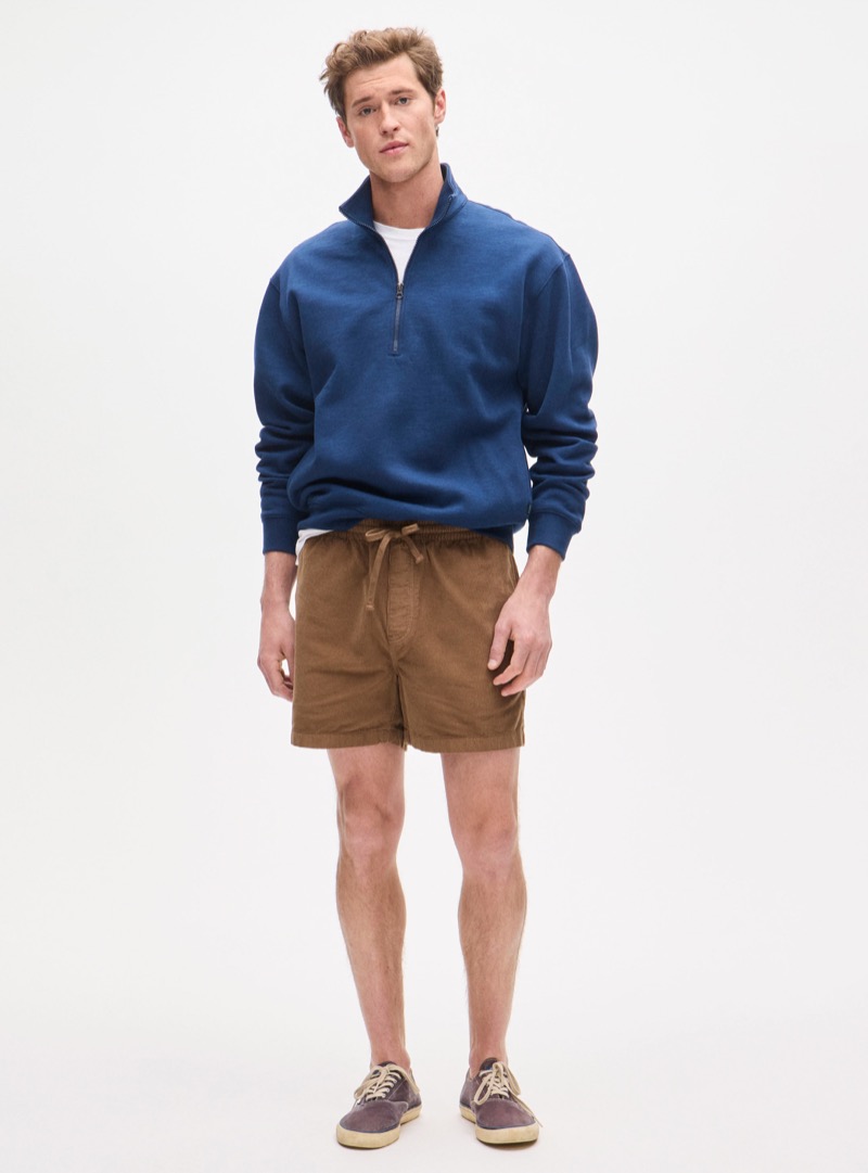 man wearing brown corduroy shorts with a blue quarter zip pullover and sneakers