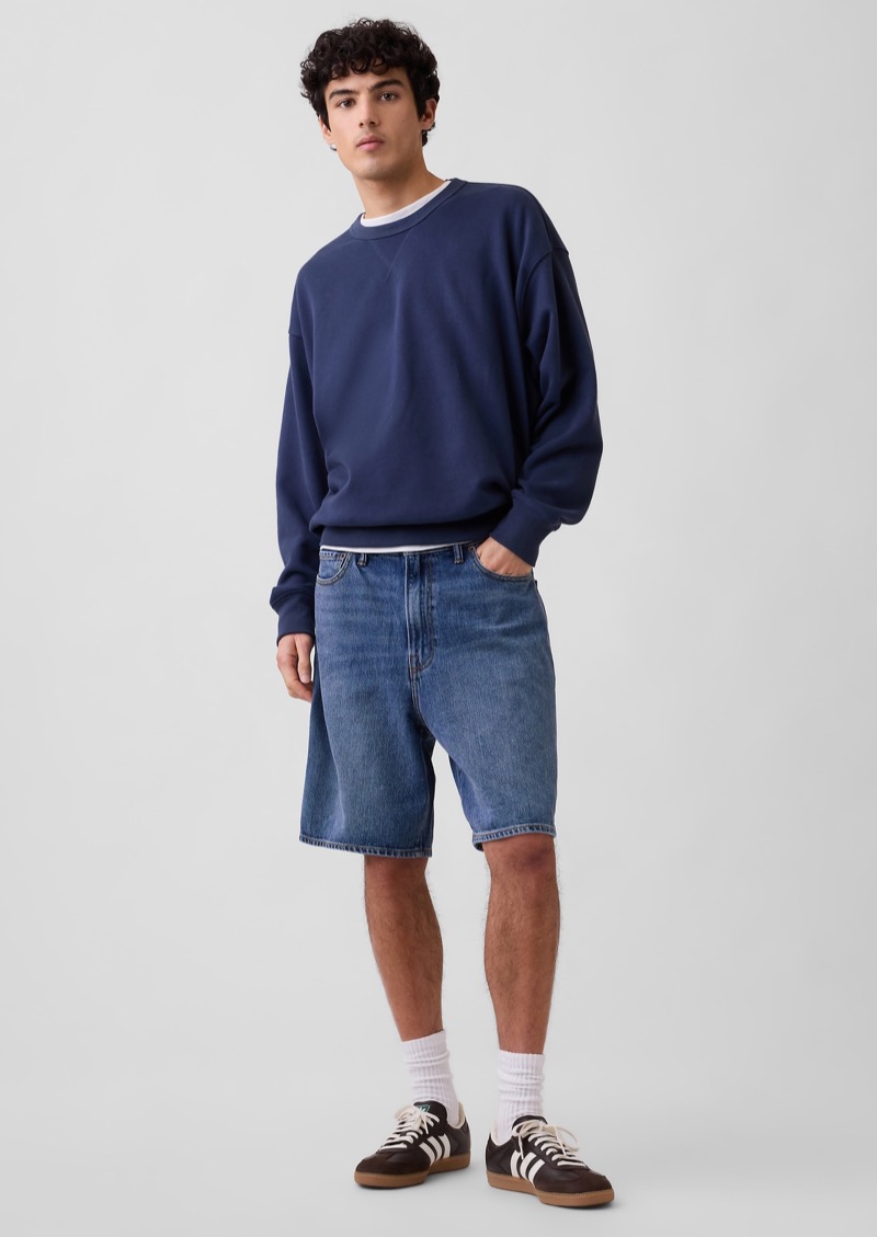 man wearing mid-wash denim shorts with a navy sweatshirt and sneakers