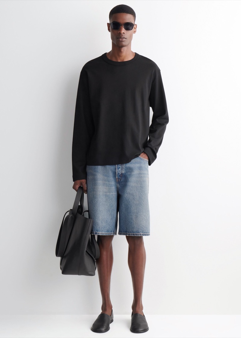 Man wearing light wash denim shorts with a black long-sleeve tee and leather loafers