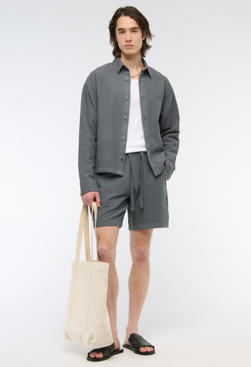 man wearing charcoal gray drawstring shorts with a relaxed fit and matching shirt with leather slide sandals