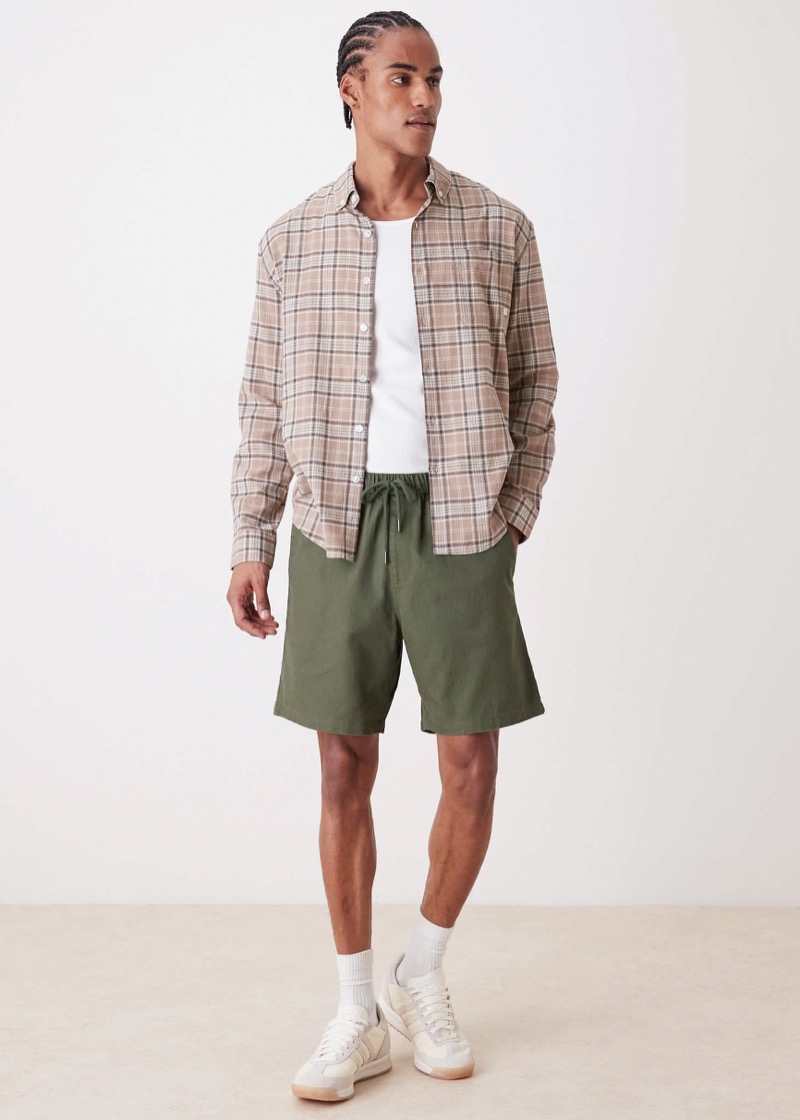 Man wearing olive green shorts with a beige plaid shirt and cream sneakers