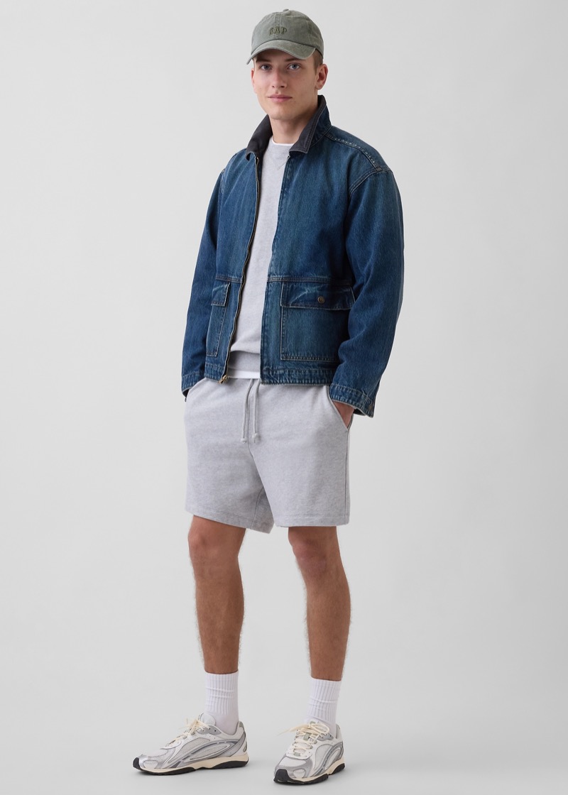 Man wearing grey sweat shorts with a denim jacket and chunky running sneakers