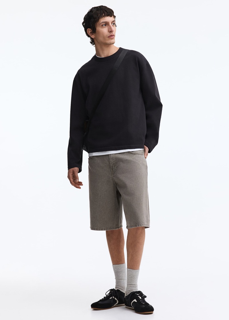 Man wearing grey washed jean shorts with a black sweatshirt and retro sneakers