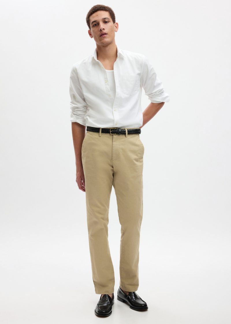 model wears white button-down shirt with khakis, a braided leather belt, and black leather loafers