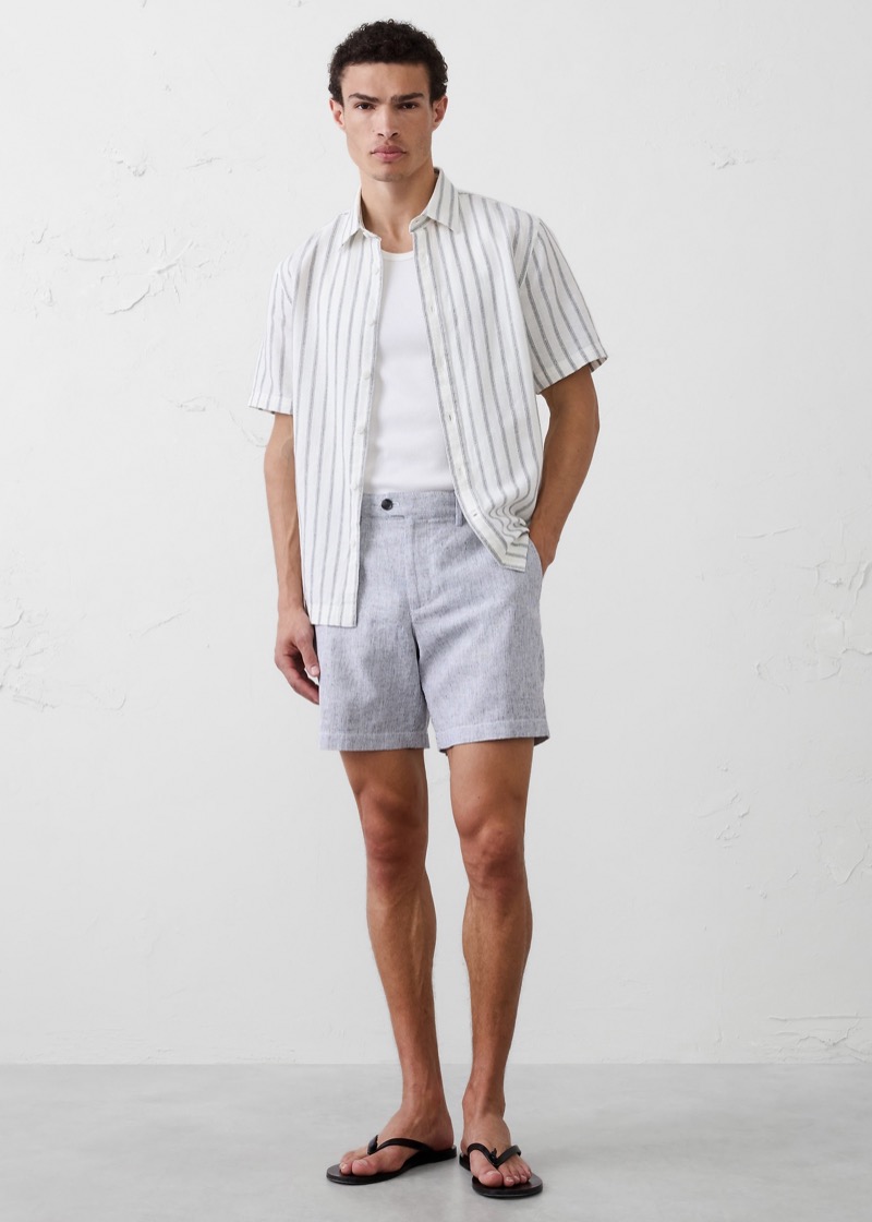Man wearing light blue linen shorts with a striped short-sleeve shirt and sandals