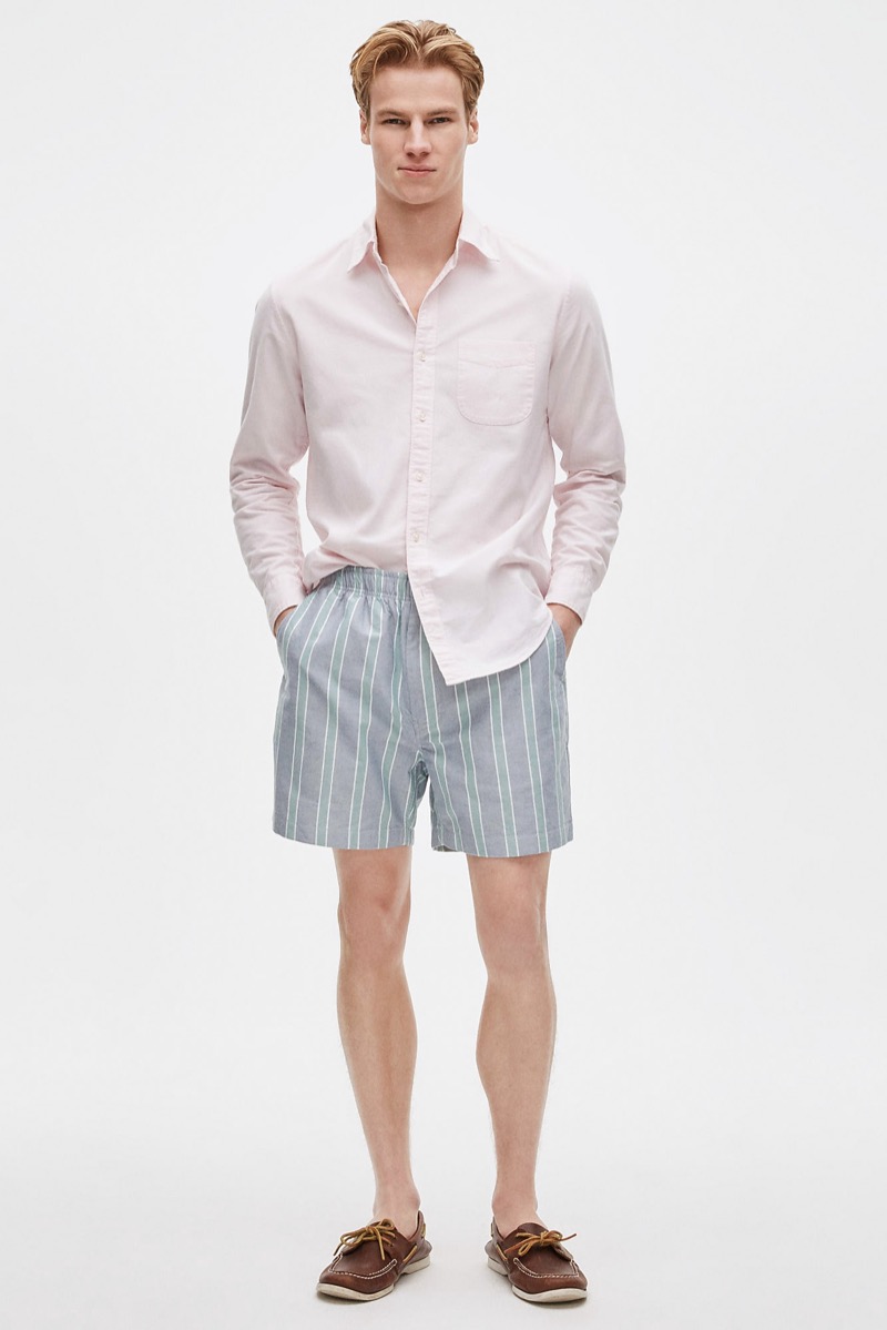Man wearing a pale pink shirt with blue and white striped elastic-waist shorts and brown leather boat shoes
