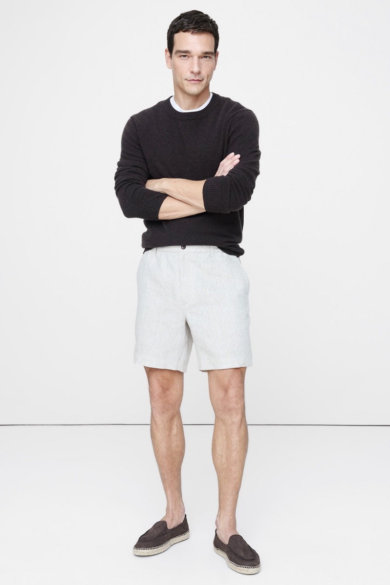 Man wearing a dark brown crewneck sweater over a white tee with stone linen shorts and dark brown suede espadrilles