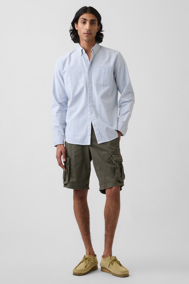 Man wearing a light blue university stripe oxford cloth button-down shirt with olive green cargo shorts and sand suede Clarks Wallabee shoes