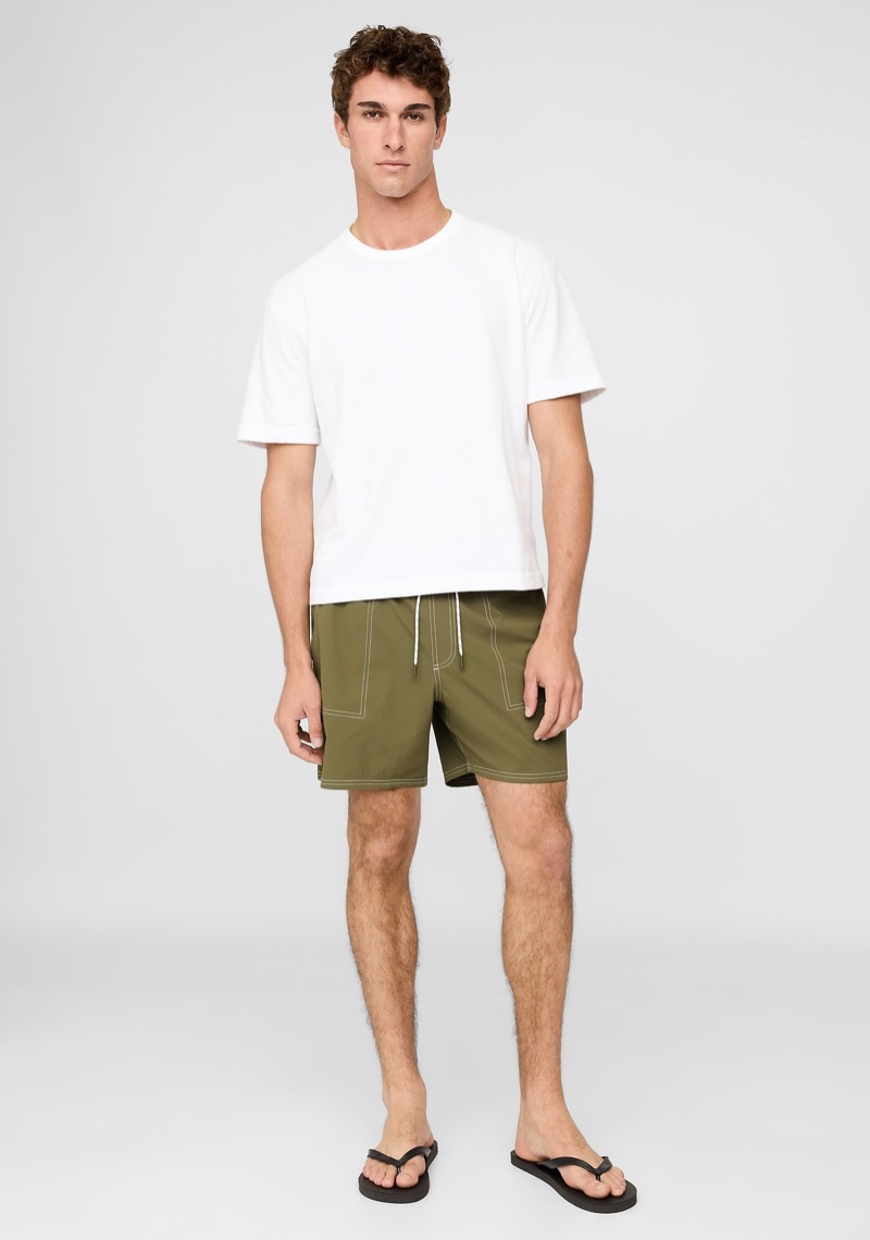 man wearing olive swim trunks with a white T-shirt and flip flops