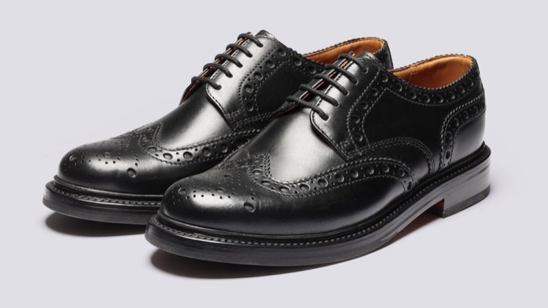 A pair of black leather full-brogue wingtip shoes with a W-shaped toe cap and decorative perforations across the vamp, quarters, and seams.