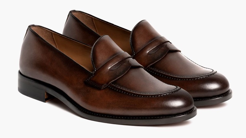 A pair of rich mahogany-brown burnished leather penny loafers with a beef-roll strap and diamond cutout across the apron, tonal stitching, and a slim leather sole with low stacked heel.
