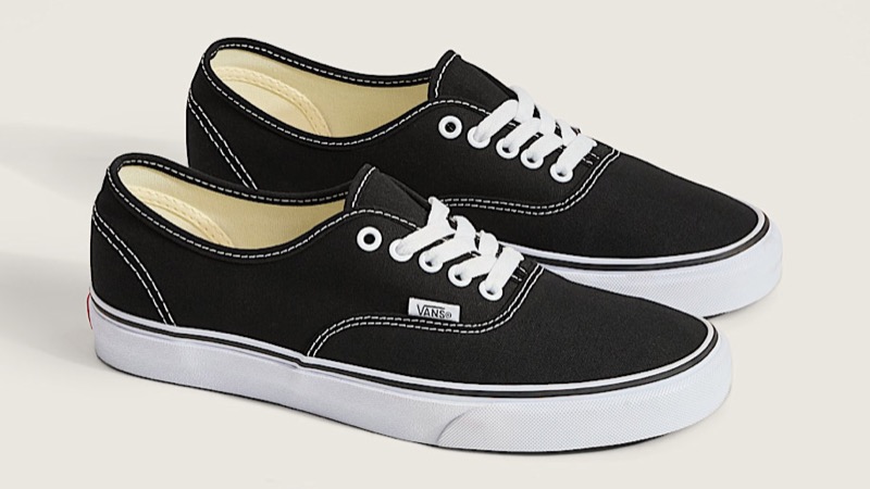 A pair of black canvas low-top skate sneakers with white contrast stitching, white laces, a white rubber foxing stripe, and a waffle-pattern vulcanized rubber sole.