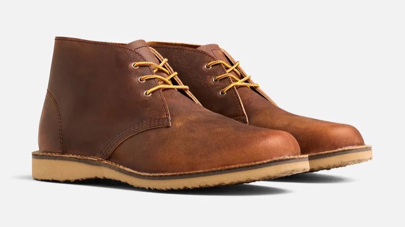 A pair of copper-brown waxed leather chukka boots with three-eyelet lacing, yellow taslan laces, and a natural crepe rubber sole.