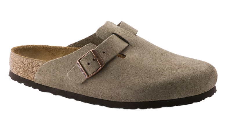 A taupe suede closed-toe clog with an adjustable buckled strap across the instep, an open back, a contoured cork footbed, and a dark EVA sole.