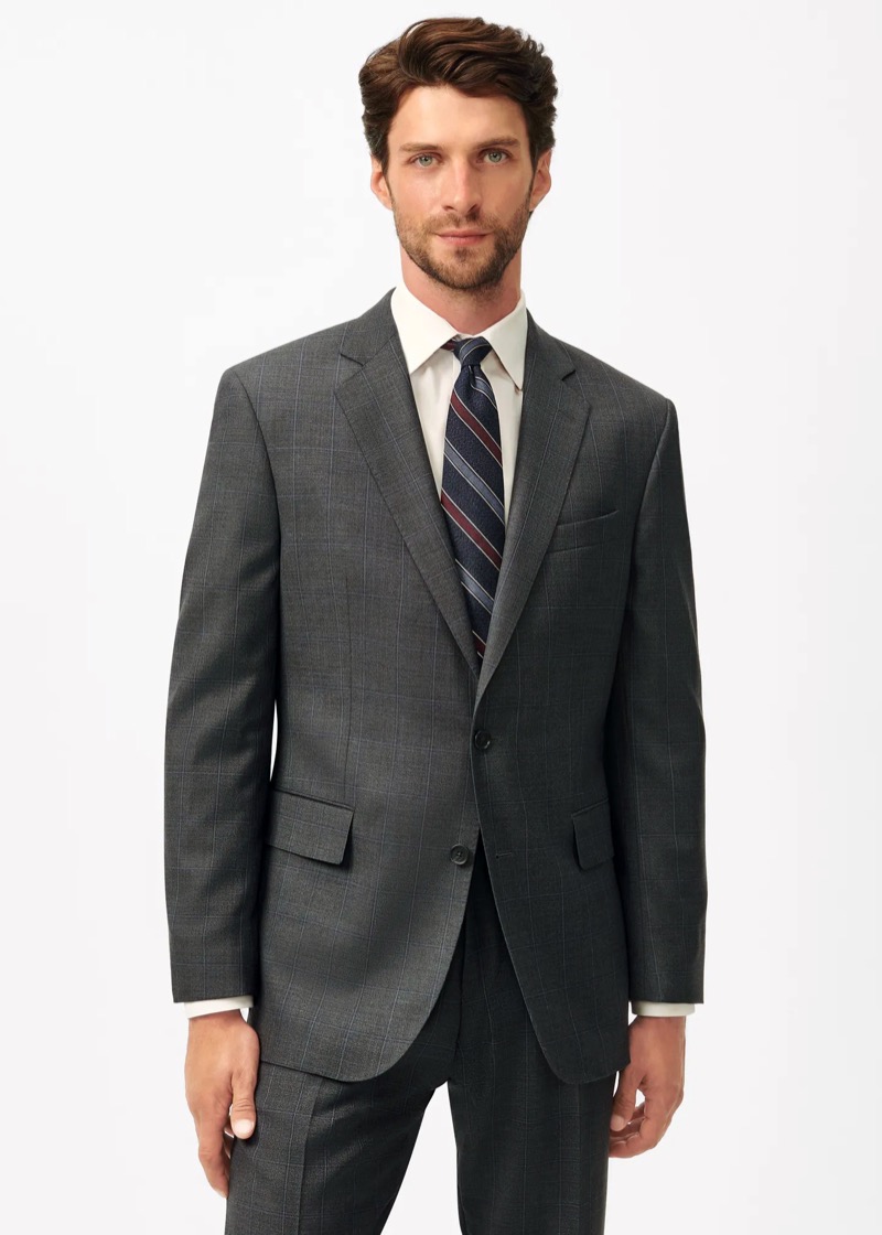 A man in a charcoal-gray windowpane-check wool suit with notch lapels and flap pockets, worn with a cream dress shirt and a navy and burgundy striped silk tie.