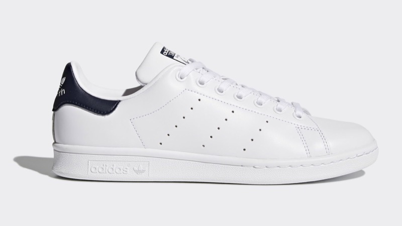 A white leather low-top court sneaker with perforated three-stripe detailing on the side, a navy heel tab, and a slim white rubber cupsole.