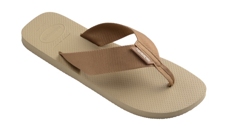A single sand-colored rubber flip-flop with a wide woven fabric Y-strap in tan, a textured footbed, and a thin rubber sole.