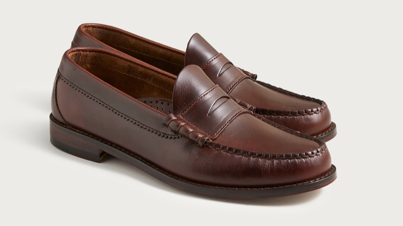 A pair of whiskey-brown leather penny loafers with a moc-stitched apron, a beef-roll strap with diamond cutout, and a slim leather sole.