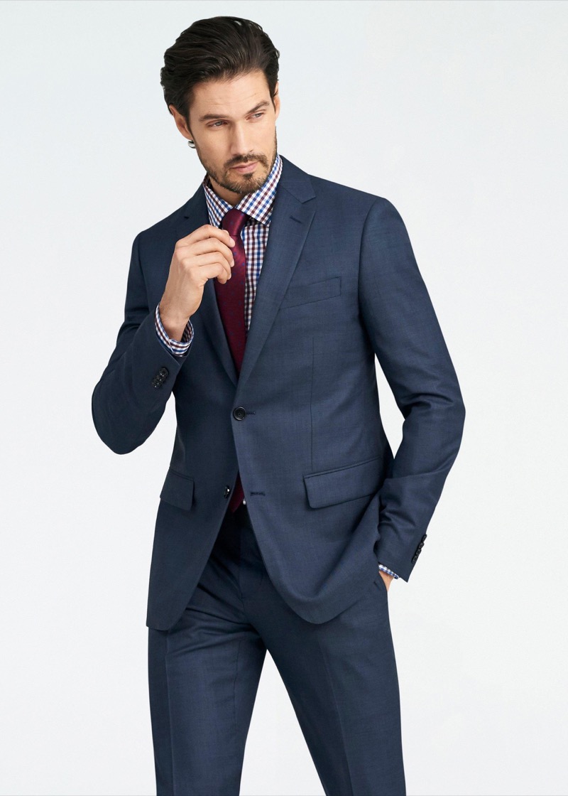 A man in a mid-navy wool two-button suit with notch lapels, paired with a burgundy and white gingham-check dress shirt and a solid burgundy silk tie.
