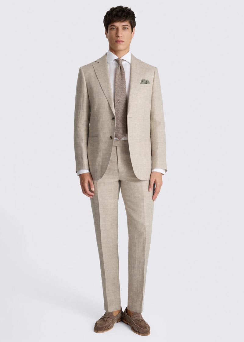 A man wearing a sand-colored linen two-button suit with notch lapels, a white dress shirt, a textured taupe knit tie, a sage-green pocket square, and brown suede woven loafers.