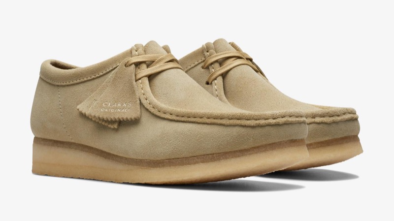 A pair of sand-colored suede Wallabees with two-eyelet lacing, a moc-toe seam running around the front, a side tongue tag, and a thick natural crepe sole.