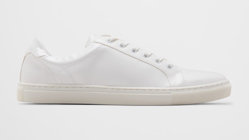 A side profile of a minimalist white leather low-top sneaker with a clean smooth-leather upper, seven-eyelet lacing, a stitched toe cap, and a slim white rubber cupsole.