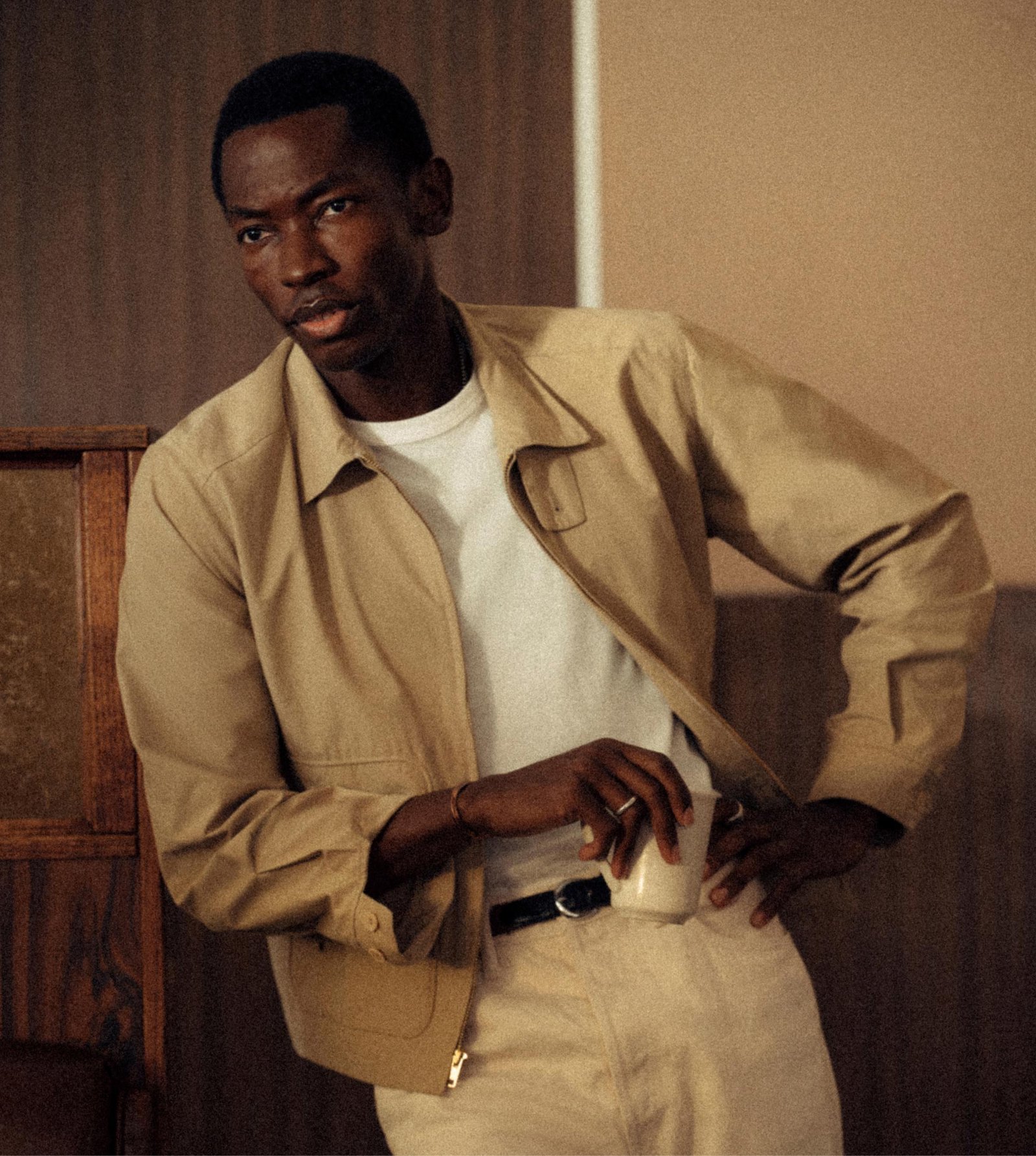 The khaki jacket pairs with an off-white tee and pale trousers.